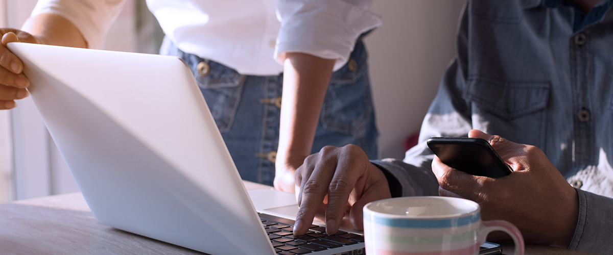 Two people with laptop computer and phone looking at devices together.